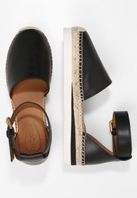 Sandalias de esparto de piel negra con suela envuelta en yute, correa ajustable en el tobillo y forro interior marrón. Detalles en costura blanca.
