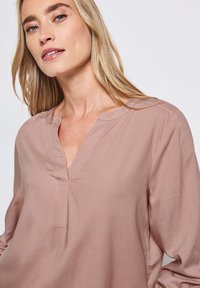 Langärmlige Bluse in Blush-Farbe mit V-Ausschnitt und subtilen Nähdetails. Glattes, leichtes Material mit lässigem Schnitt.