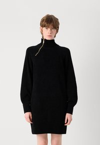 Černé svetr šaty z měkké pleteniny. Obsahují vysoký límec s diagonálním zlatým zipem, žebrované manžety a lem. Oversized střih s dlouhými rukávy.