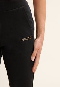 Pantalones jogger negros con una textura suave y una silueta ajustada. Logo "FREDDY" adornado con piedras de strass en el lado izquierdo. Cintura con elastano.