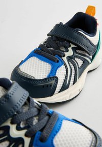 Buty sportowe wykonane z siateczki i materiałów syntetycznych, z ciemnoniebieskimi, białymi i zielonymi akcentami, z regulowanymi paskami i teksturowanymi podeszwami.