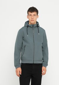 Grau Zip-Hoodie mit Kapuze, ausgestattet mit verstellbaren Kordeln, seitlichen Taschen und gerippten Bündchen, aus einem glatten, dehnbaren Material gefertigt.