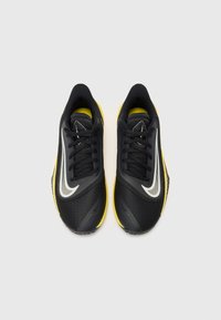 Chaussures de sport noires avec semelle jaune, dotées d'un dessus texturé, d'accents blancs et d'un design traditionnel à lacets.