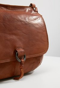 Brun læder messenger taske med en glat tekstur, stor klaplukning, metalkrængs accent og en side detalje med læderrem.