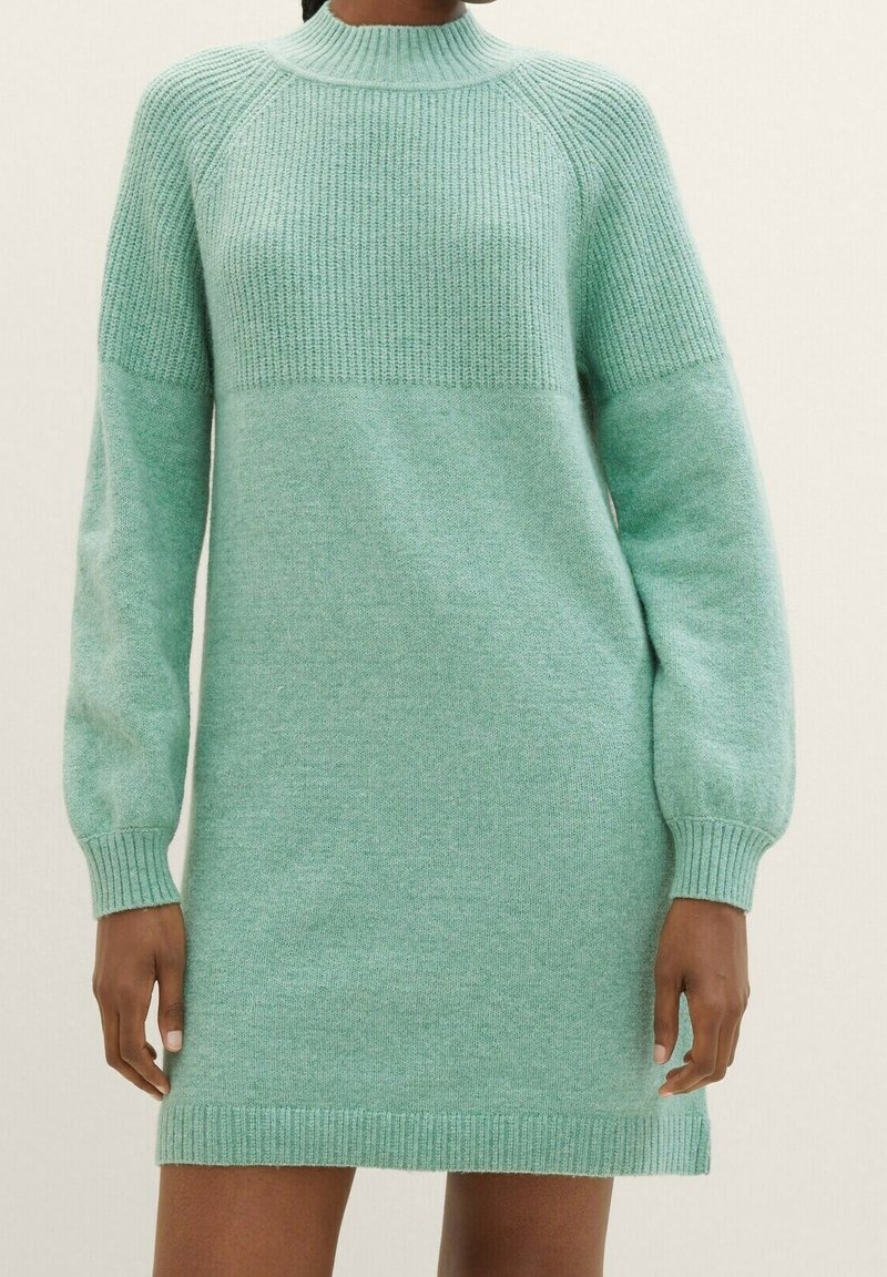 Robe-pull tricotée vert menthe à col montant côtelé, manches longues et poignets ajustés, portée par une personne debout sur un fond uni.