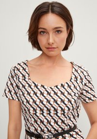 Musterkleid mit quadratischem Ausschnitt, kurzen Ärmeln und einer Mischung aus schwarz, weiß und braun in Wellenmustern; tailliert mit einem schwarzen Gürtel.
