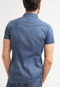 Kortärmad denimskjorta i mörkblått. Har spetsig krage, rundad yoke-detalj och en slim fit-design. Slät textur.