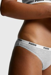Grauer Baumwolltanga mit einem weißen Bund, der mit schwarzem "PUMA"-Branding versehen ist. Glatte Textur und schlichtes Design, geeignet für den täglichen Gebrauch.