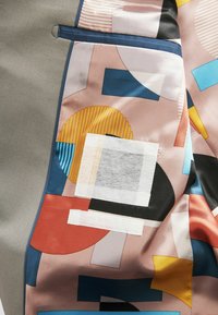 Tejido estampado que presenta formas geométricas en colores como rosa, azul, amarillo y negro. Textura suave con una mezcla de acabados mate y brillante.