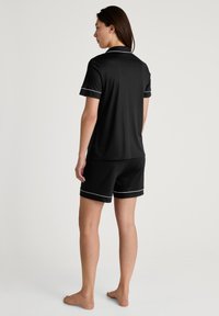 Zwarte pyjama set met een T-shirt met korte mouwen en korte broek met witte piping accenten. Zachte stof, casual pasvorm en ontspannen silhouet.