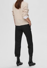 Maglione beige a maglia con maniche arrotolate, abbinato a pantaloni neri aderenti e stivaletti neri alla caviglia. Texture morbida e vestibilità casual.