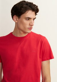 T-shirt rossa in cotone con scollo a girocollo e maniche corte. Presenta una stampa del logo sottile sul davanti. Texture liscia e vestibilità comoda.