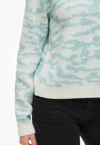 Maglione azzurro chiaro e bianco con una texture morbida e soffice, caratterizzato da un delicato motivo a nuvole e orlo a costine, abbinato a pantaloni neri.