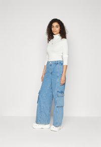Lys blå denim cargo bukser med store lommer, brede ben og en let slidt detalje, parret med en hvid ribbet turtle-neck.