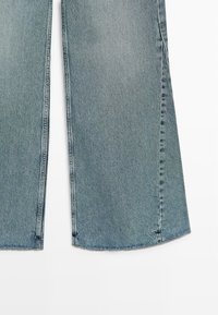 Lichtblauwe spijkerbroek met wijde, uitlopende pijpen en zichtbare verticale stiksels langs de buitennaden, op een witte achtergrond.