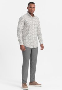 Blomstermønstret skjorte i lyse farver, parret med grå skræddersyede bukser og beige sneakers, med et klassisk kravedesign.