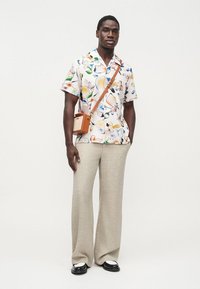 Κοντομάνικο, κρεμ πουκάμισο με πολύχρωμα μοτίβα φρούτων· συνδυασμένο με μπεζ ανοιχτόχρωμο παντελόνι φαρδιάς γραμμής και μαύρα παπούτσια με λευκές λεπτομέρειες. Καφέ τσάντα χιαστί.