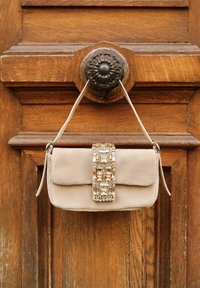 Sac à main en daim beige avec un fermoir rectangulaire orné de pierres décoratives. Il possède un rabat et une seule bandoulière.
