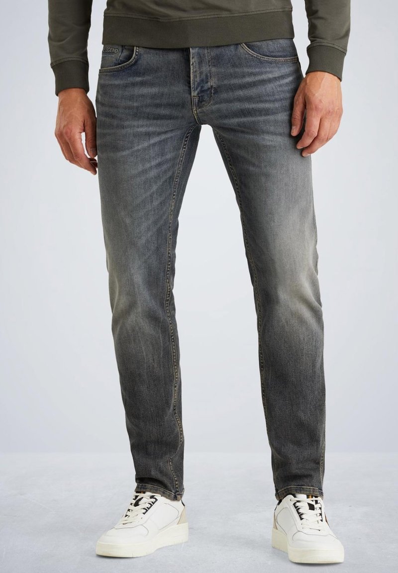 Jeans en denim gris à coupe slim, avec un délavage, un design à cinq poches, et des accents beiges sur des baskets blanches.
