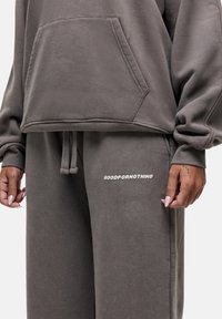 Grijze oversized hoodie met een voorzak en bijpassende joggingsbroek. Kenmerkt zich door witte tekst "GOODFOR NOTHING" op de broek. Zacht, textuurstof.