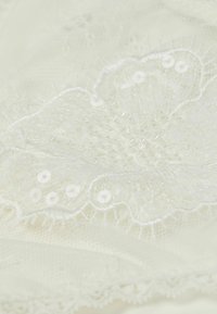 Kantstof in off-white met geborduurde bloempatronen, pailletten en kralen; getextureerd met ingewikkelde details en delicate randen.