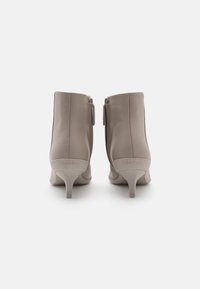 Botas de tobillo de cuero taupe con punta afilada, tacón delgado y cierre de cremallera. Nombre de la marca "Calvin Klein" grabado en el tacón.