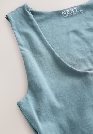 Tunika sa izrezom u obliku žlice od svijetloplavog tkanja, s mekanom teksturom i bez rukava. Oznaka glasi "NEXT."