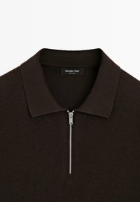 Polo en maille marron foncé avec une fermeture éclair argentée sur le devant et une étiquette "Massimo Dutti" à l’intérieur du col.