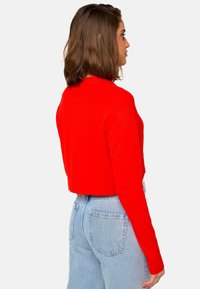 Pull court rouge à manches longues, présentant un design simple et des poignets côtelés, associé à un jean bleu clair taille haute.