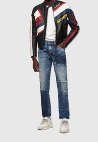 Svart lädermotorcykeljacka med röda, vita och blå ränder, i kombination med lapptäckta blå jeans och vita sneakers.