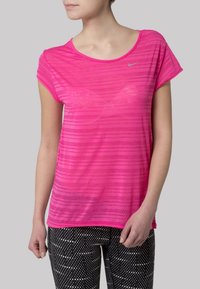 Růžové pruhované sportovní tričko s krátkými rukávy, kulatým výstřihem a reflexním logem. V kombinaci s legínami s černými puntíky.