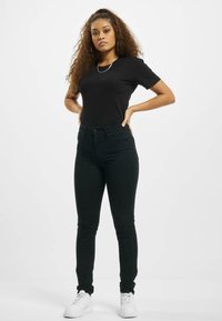 Svart tettsittende t-skjorte kombinert med høyt liv svarte jeans og hvite joggesko, med glatte teksturer og enkelt design.
