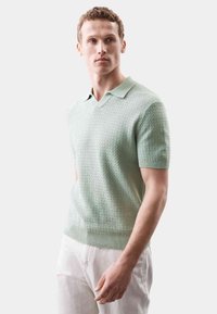 Polo s krátkým rukávem a V-výstřihem v mátově zelené barvě, vyrobený z texturované pleteniny, s žebrovaným lemem a límcem pro přiléhavější vzhled.