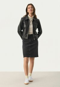 Schwarze Lederjacke mit zwei Vordertaschen, kombiniert mit einem schwarzen Jeansrock. Weiße Sneaker und hellfarbige Socken vervollständigen das Outfit.