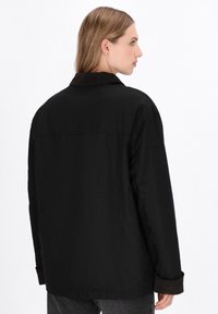 Jachetă neagră cu guler din catifea, croi lejer, mâneci lungi și material texturat. Prezintă un design simplu și minimalist.