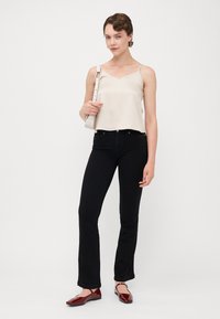 Beige satinkamisol, svarta utsvängda jeans och vinröda ballerinas. Modellen håller en vit axelremsväska. Enkla och rena linjer genomgående.