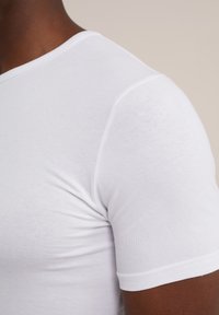 Witte katoenen T-shirt met korte mouwen, ronde halslijn, gladde textuur en zichtbare stiksels langs de schoudernaad.