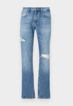 Svijetloplave traperice ravnog kroja. Imaju izlizane dijelove na koljenima i suptilno izbjeljivanje. Zatvaranje na jedan gumb s petljama za remen.