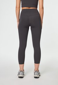 Leggings de cintura alta ajustados en gris oscuro, hechos de una tela elástica con una textura suave. Llevados con zapatillas deportivas grises.