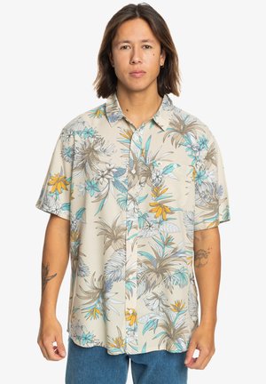 Short-sleeve shirt in light beige fabric featuring a tropical floral pattern in turquoise, yellow, and brown. Button-down design with pocket.