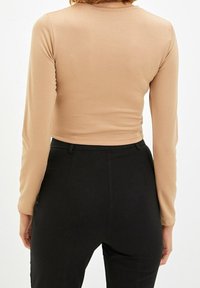 Beige eng anliegendes Langarm-Crop-Top mit glatter Textur, Rundhalsausschnitt und nahtlosem Design, kombiniert mit hochgeschnittenen schwarzen Hosen.