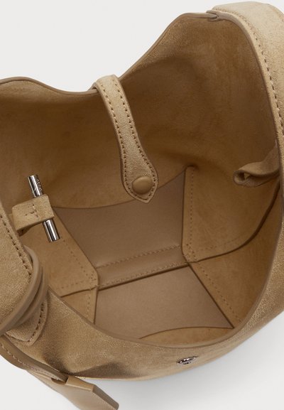 Εσωτερικό μπεζ τσάντας από σουέτ με κλείσιμο με κουμπί, διαθέτοντας λεία υφή και απλό σχέδιο. Περιλαμβάνει μεταλλικό τόνισμα στην επένδυση.