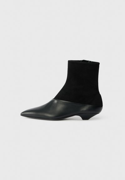 Bottine noire avec une tige en daim texturé et un embout en cuir lisse. Dispose d'un bout pointu et d'un design de talon bas unique.