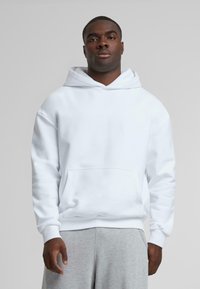 White hoodie featuring a kangaroo pocket, drawstring hood, and ribbed cuffs, paired with gray sweatpants. Smooth texture, casual design.