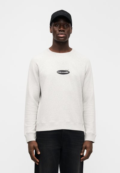 Gray fleece sweatshirt with a round neckline and ribbed cuffs, featuring a black "VOLTAIRE" logo. Paired with dark jeans and a black cap.
