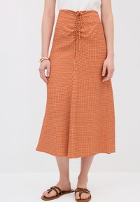Falda midi de cuadros marrón con cintura fruncida, que presenta un cordón ajustable. Tejido suave con forma acampanada, combinada con sandalias marrones.