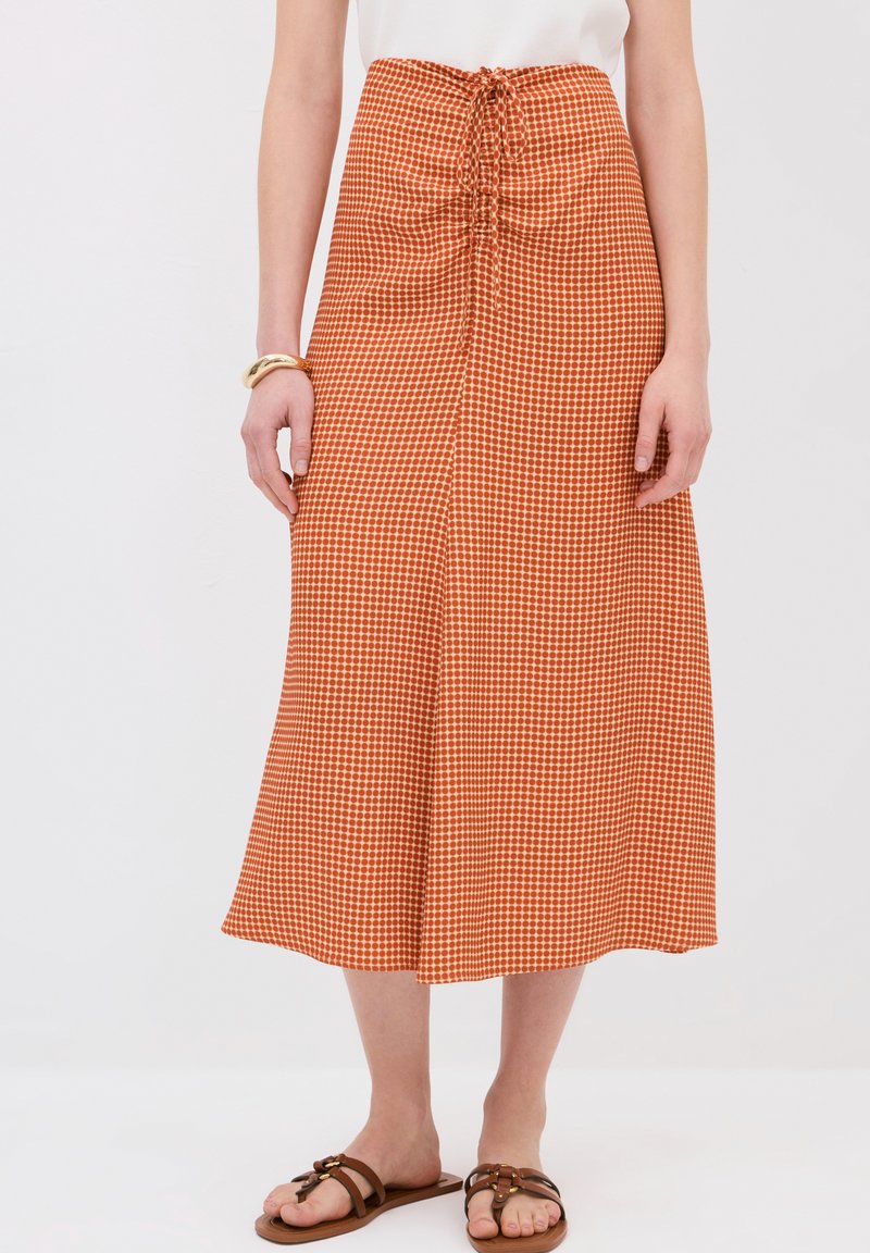 Falda midi de cuadros marrón con cintura fruncida, que presenta un cordón ajustable. Tejido suave con forma acampanada, combinada con sandalias marrones.