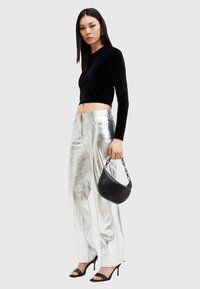 Fekete bársonyból készült, hosszú ujjú crop top, fémes ezüstszínű nadrág, fekete láncos kézitáska, nyitott orrú fekete magassarkú szandálok, sima textúrák.