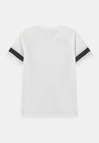 Vit idrottströja med textilstruktur, korta raglanärmar och svarta ränder på ärmarnas kanter. Har en öppning i nackpartiet bak.