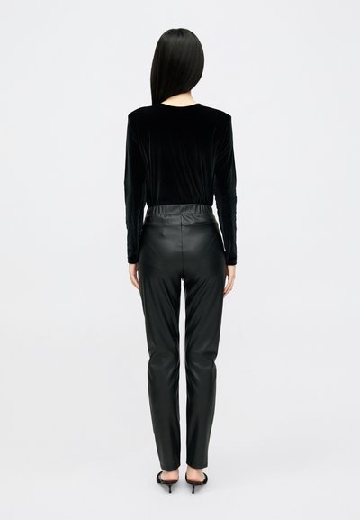 Top lung cu mâneci lungi din catifea neagră și pantaloni din piele neagră cu talie înaltă, ajustați pe picior, cu un luciu subtil și fără modele sau accesorii vizibile.